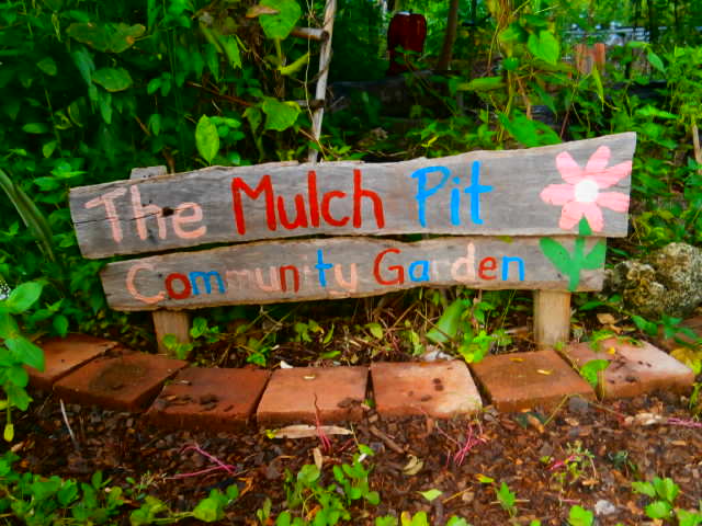 Wooden sign in a garden bed that says “The Mulch Pit Community Garden”